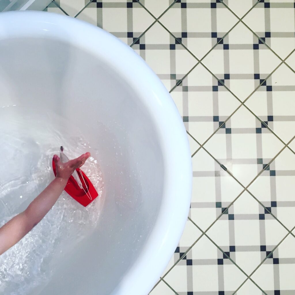Enfant qui joue avec un petit bateau en bois de la Maison Tirot dans une baignoire